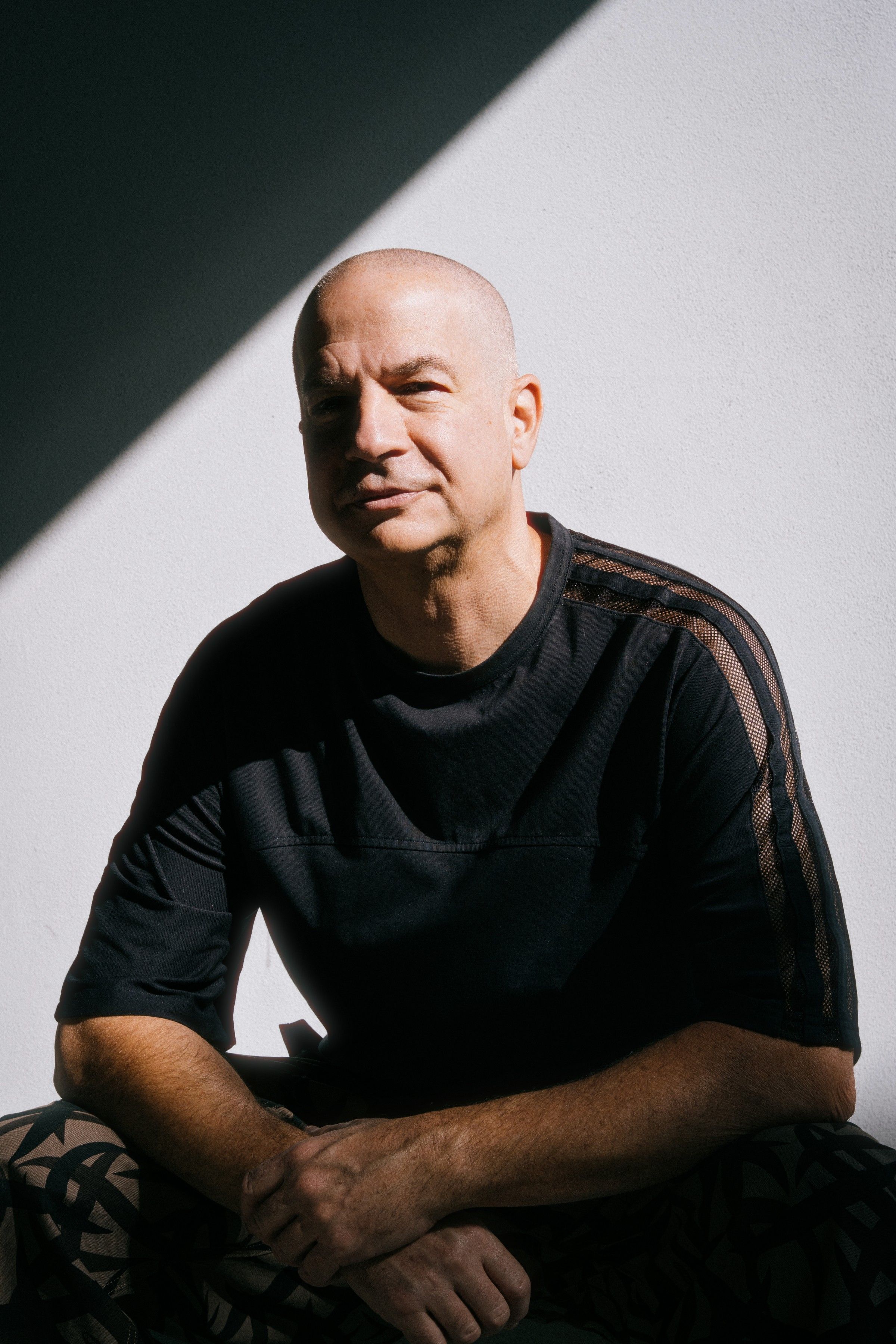 Murat Uncuoglu seated against a white wall, cut by a diagonal band of shadow